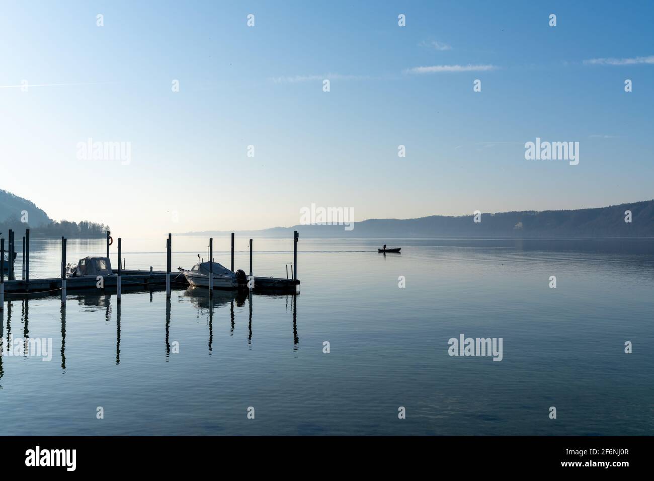 A view of a calm blue lake with moored ships and a small motorboat cruising through the water Stock Photo