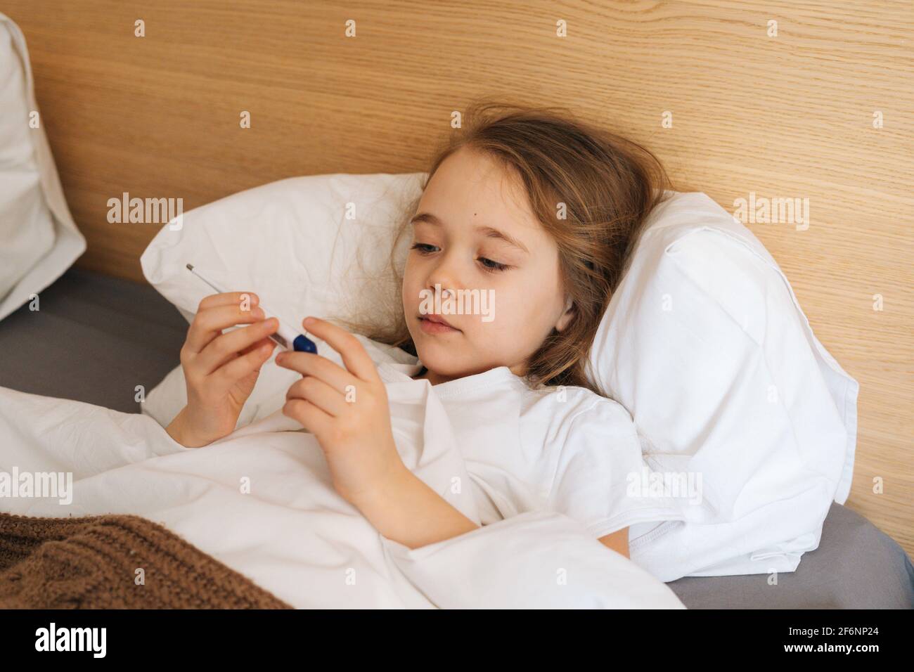 Closeup face of cute little sick girl with high fever lying under