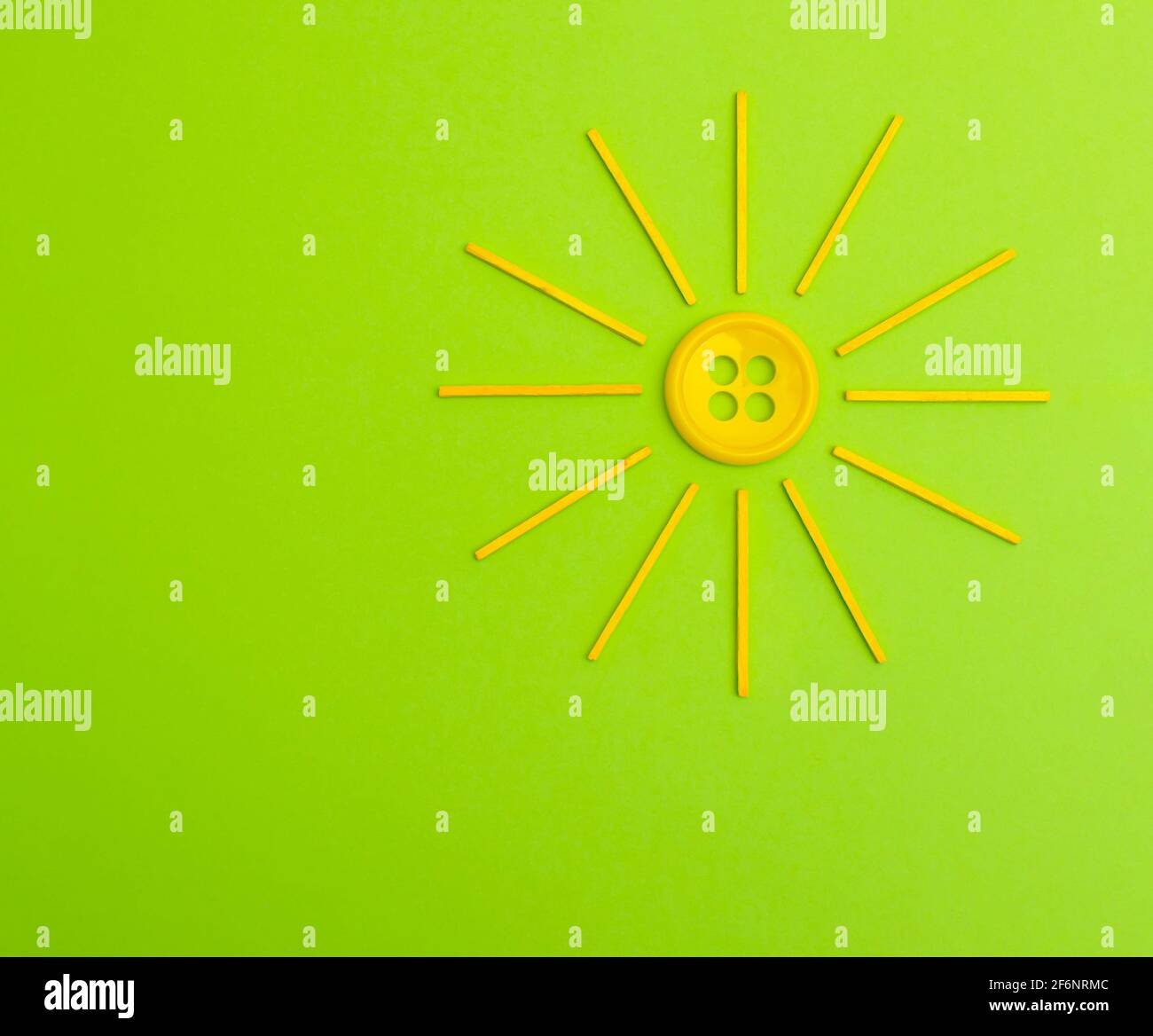 Stylized Yellow sun made from button and wood sticks on a green background. Creative spring flat lay. Stock Photo