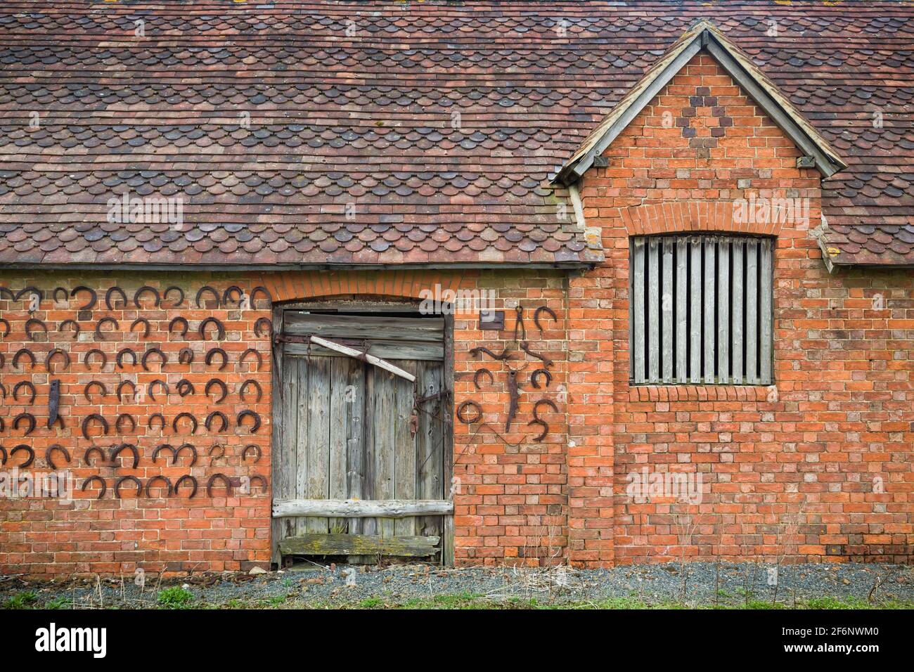 BUCKINGHAM, UK - April 05, 2015. Old brick farm building or outbuilding with wooden barn door wall decorated with horseshoes, UK Stock Photo