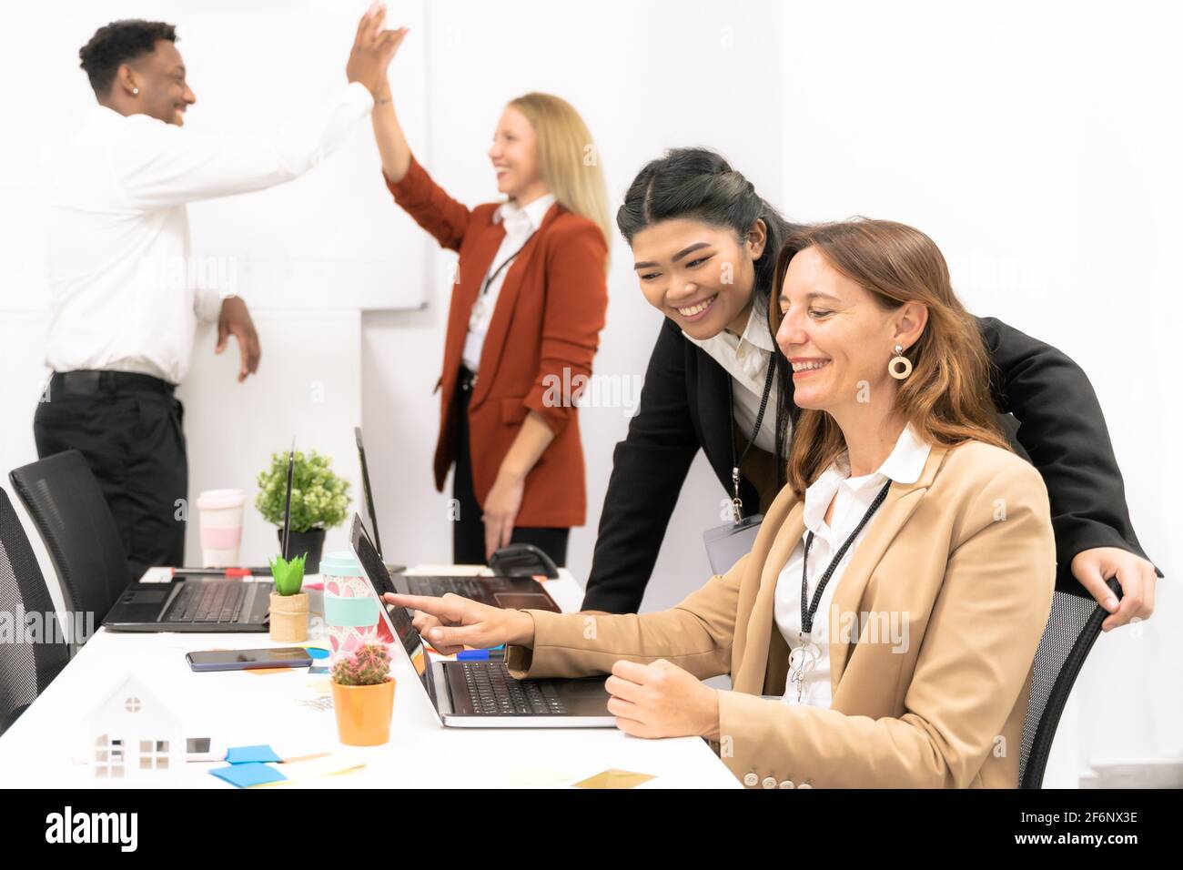 Group of multiracial business people working and communicating while sitting at the office desk together with colleagues high fiving in the background Stock Photo