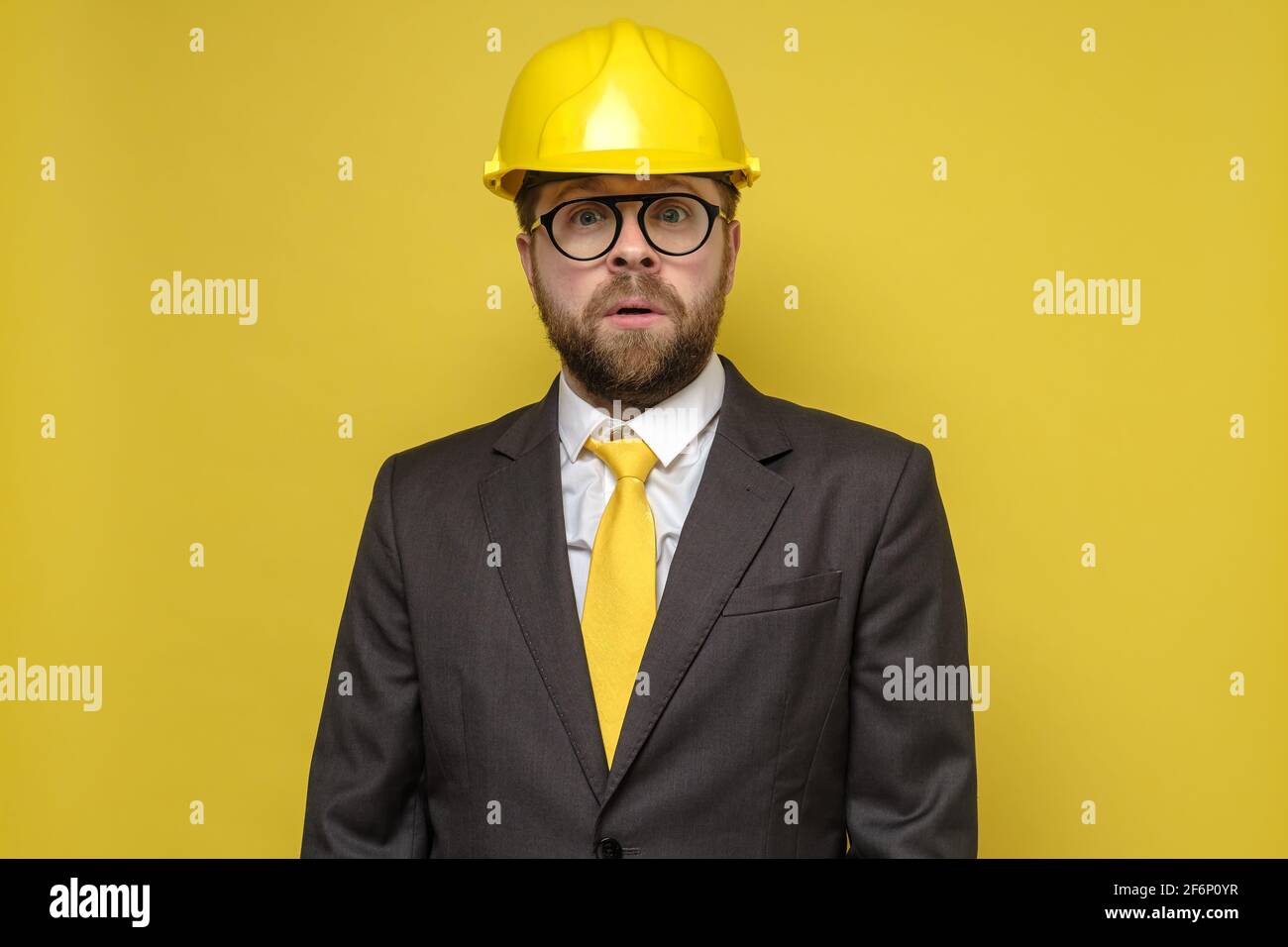 Surprised man in a construction helmet and a suit anxiously looks into the camera with big eyes and mouth open.  Stock Photo