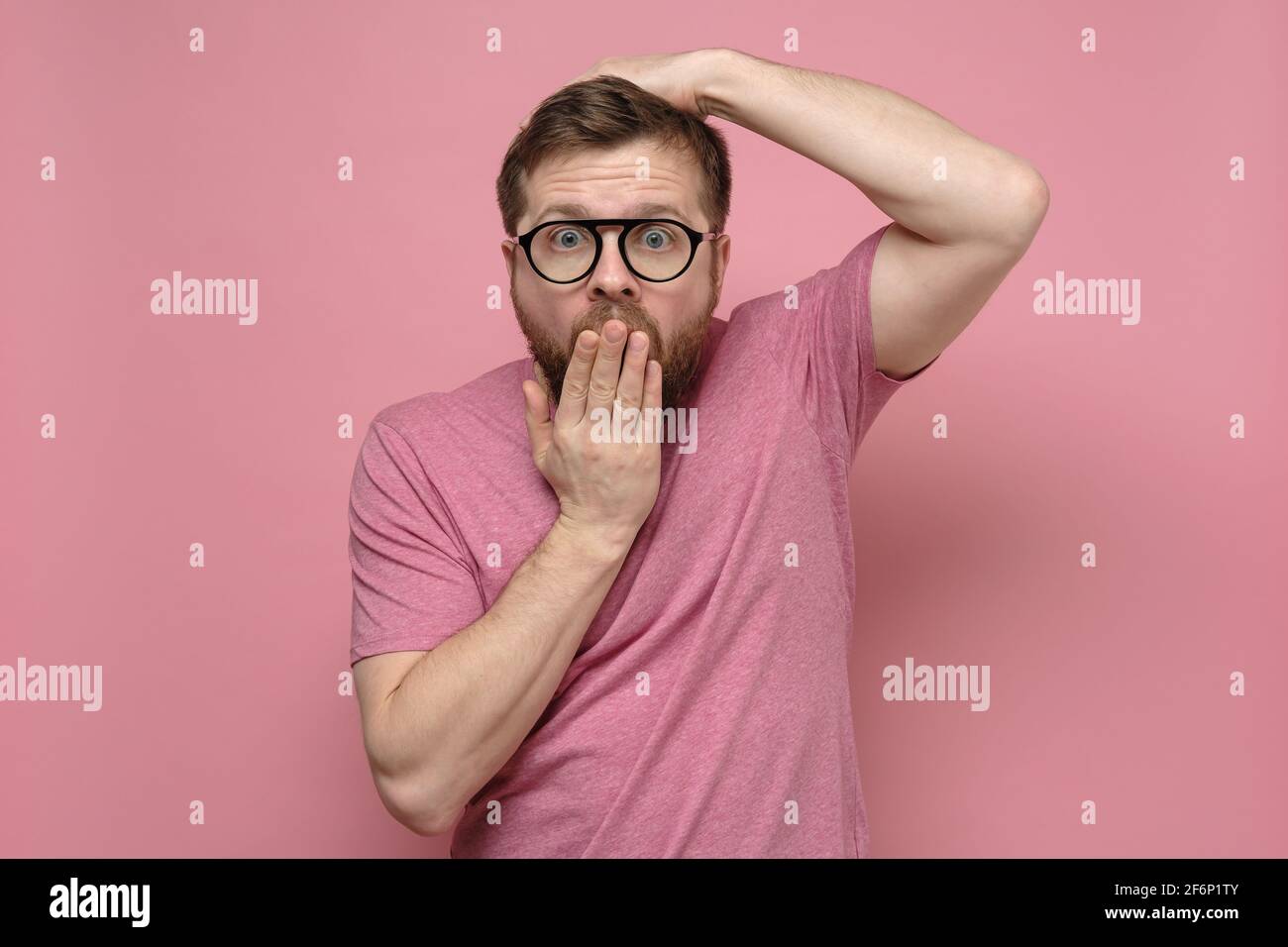 Shocked, strange man with glasses in fright covers mouth with one hand