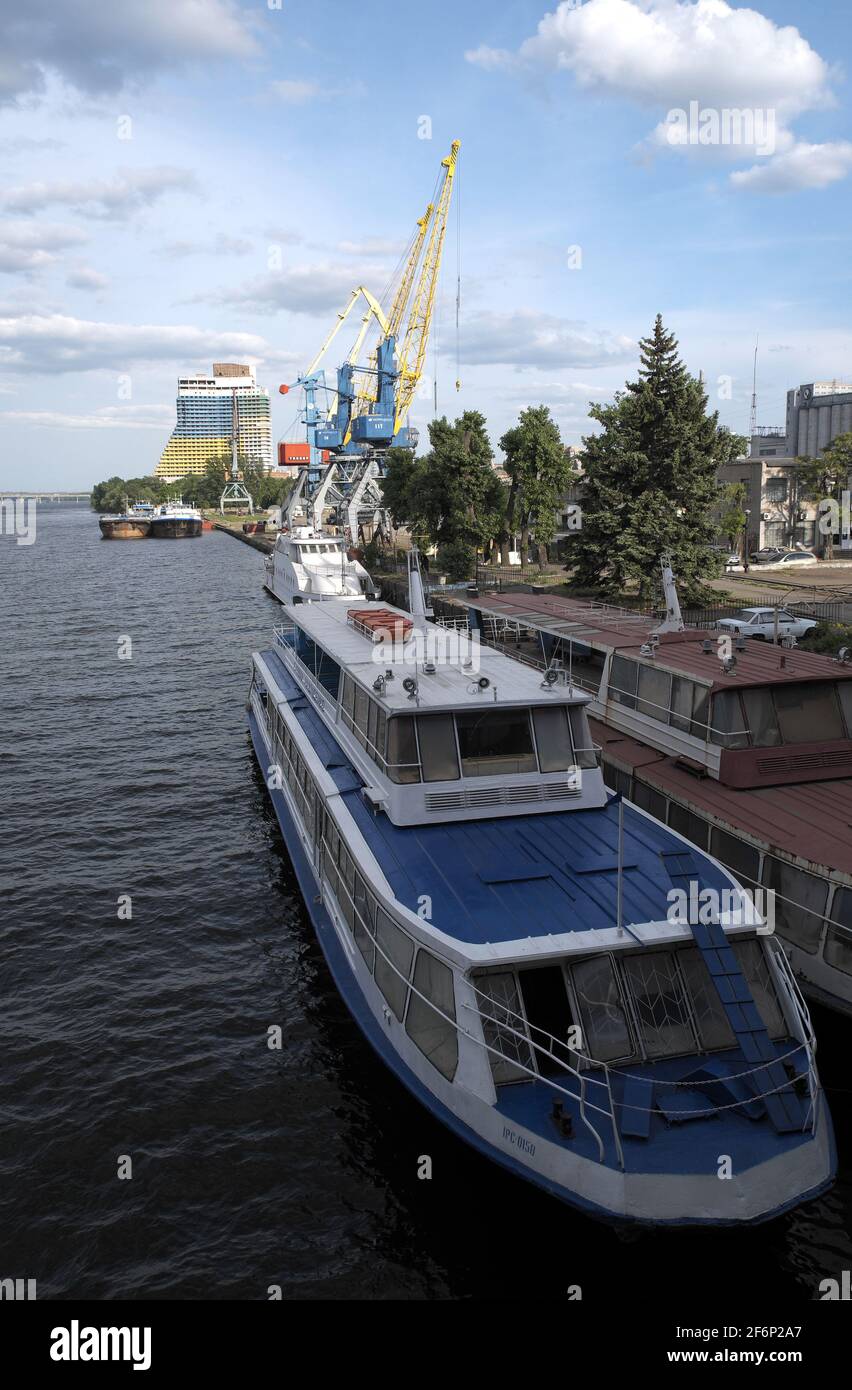 River cruise boats moored beside quayside, with cranes and an apartment block beyond, River Dnieper, Dnipro, Ukraine. Stock Photo