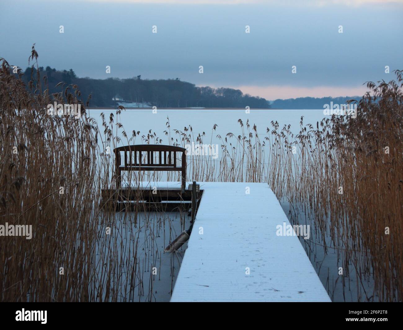 Bathing Pier with Bench and Reed in winter morning in Winter Snow at Frozen Lake Stock Photo
