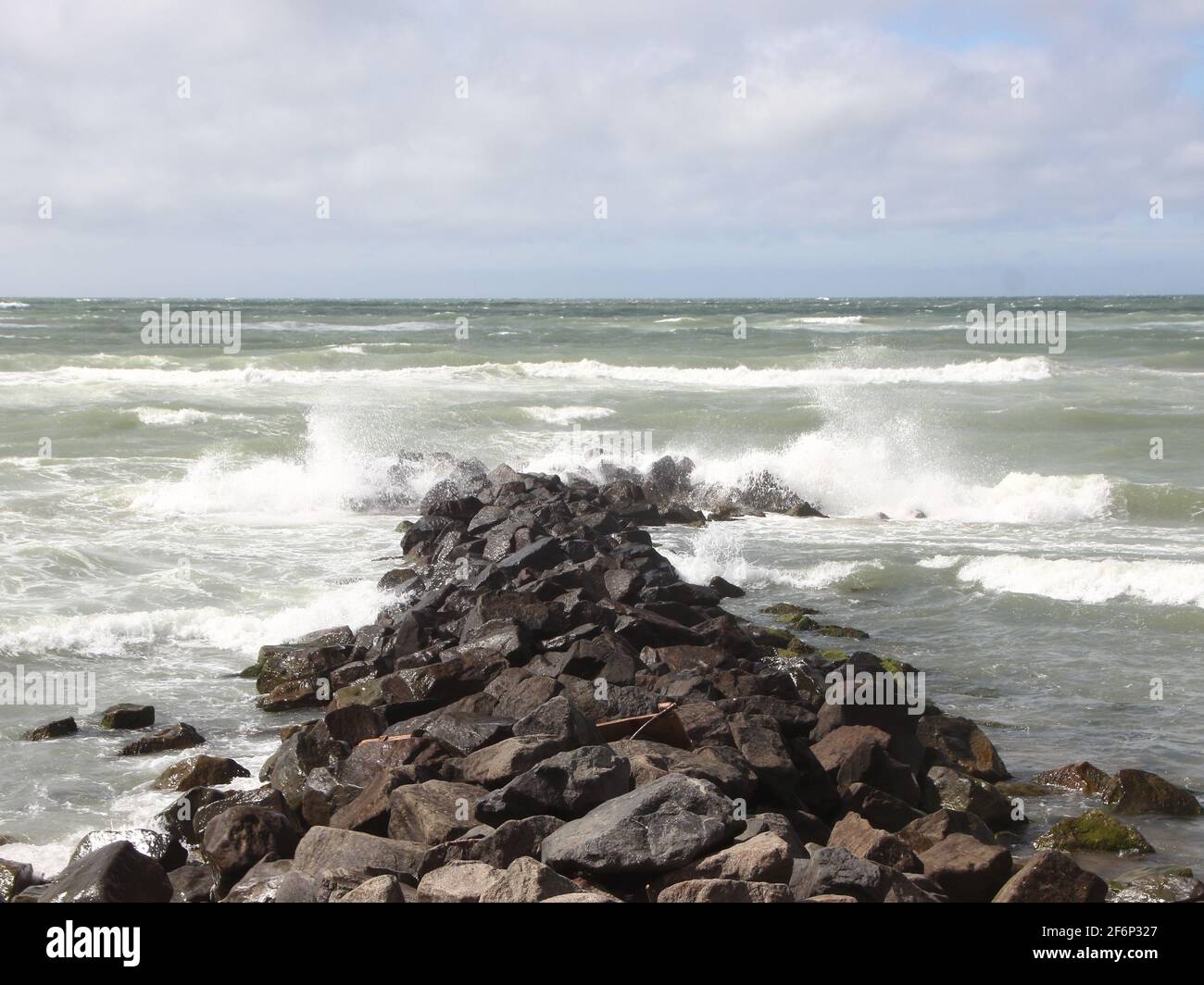Solid breakwater rocks in line with cloudy ocean horizon Stock Photo