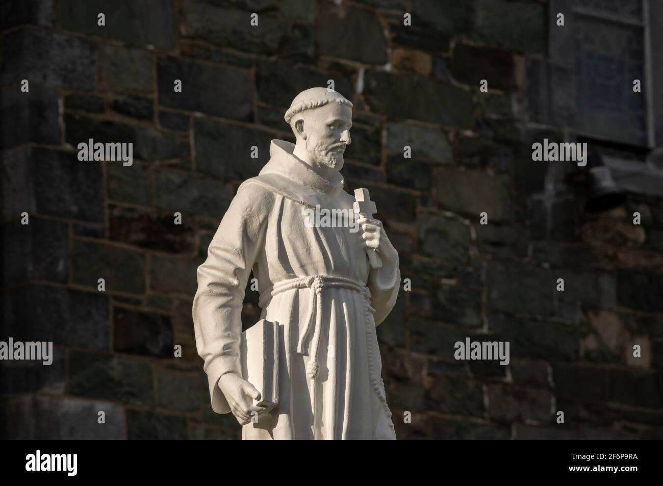 Religious figure holding a holy cross and book against church stone