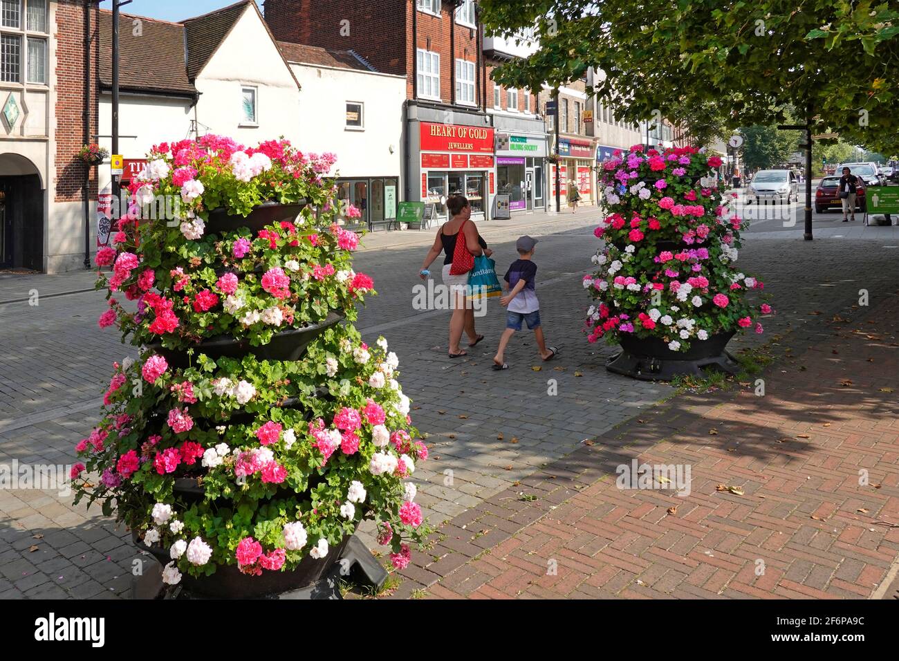 Mother holding Covid 19 coronavirus face mask in hand walking with young boy summer flowers in almost deserted Brentwood shopping High Street Essex UK Stock Photo