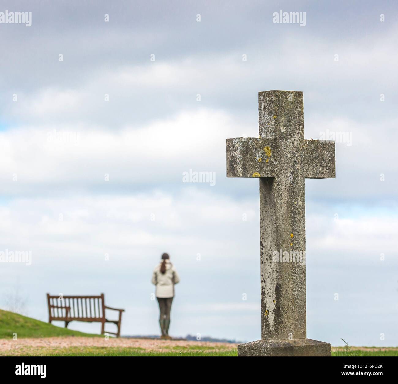 Stourbridge, UK. 2nd April, 2021. with Covid-19 suddenly changing our entire way of life over the past twelve months, this Good Friday is a time for many to reflect upon life and prepare for a better future. A visitor to a quiet churchyard can be seen having a silent moment of contemplation whilst looking out on to a country landscape, deep in thought.  Credit: lee Hudson/Alamy Live News Stock Photo