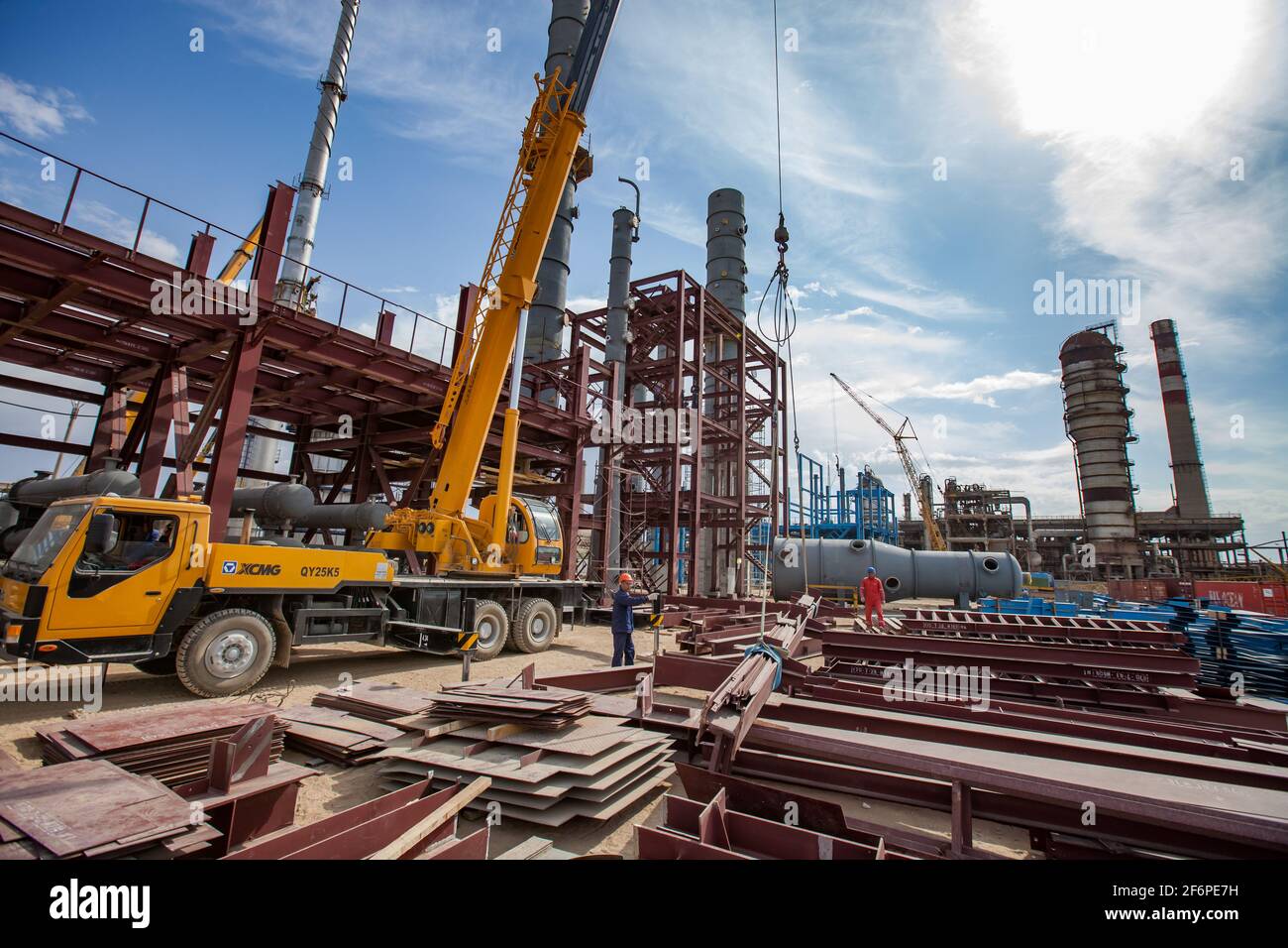 Aktau, Kazakhstan - May 19, 2012: Construction of asphaltic bitumen plant refinery column. Metal distillation tower and yellow hydraulic hoist. Stock Photo