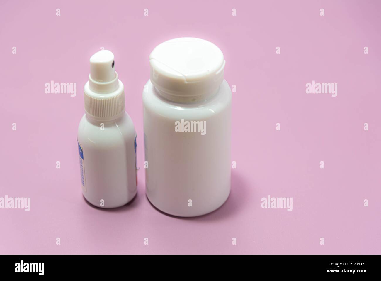Medical plastic spray bottles and pills on pink background. Medicine