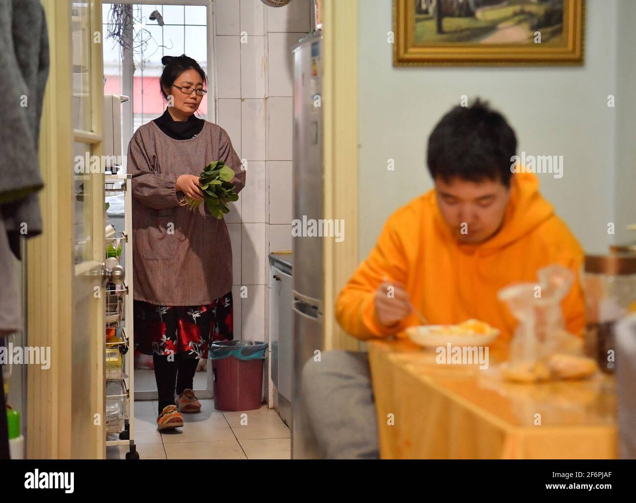 (210402) -- TIANJIN, April 2, 2021 (Xinhua) -- Wu Guixiang does house chores as her son Zhang Hao, diagnosed with autism, finishes his dinner in Hebei District, north China's Tianjin, March 29, 2021.  In 1998, Zhang Hao was diagnosed with autism at the age of two. Ever since the diagnosis, Zhang's mother Wu Guixiang has spent all her time looking after her son.    In order to help Zhang Hao and eight others with autism improve their social engagement after they had become grown-ups, Wu set up an autism training center in 2016, providing them with courses on life, social and vocational skills. Stock Photo