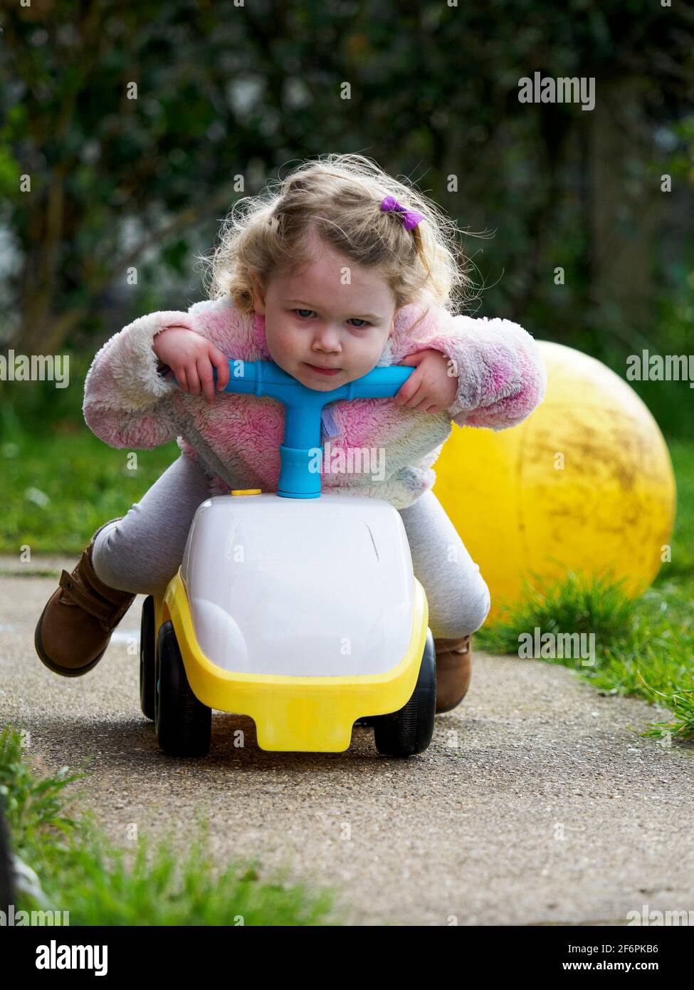 Toddler playing on a ride on toy car in the garden, UK Stock Photo