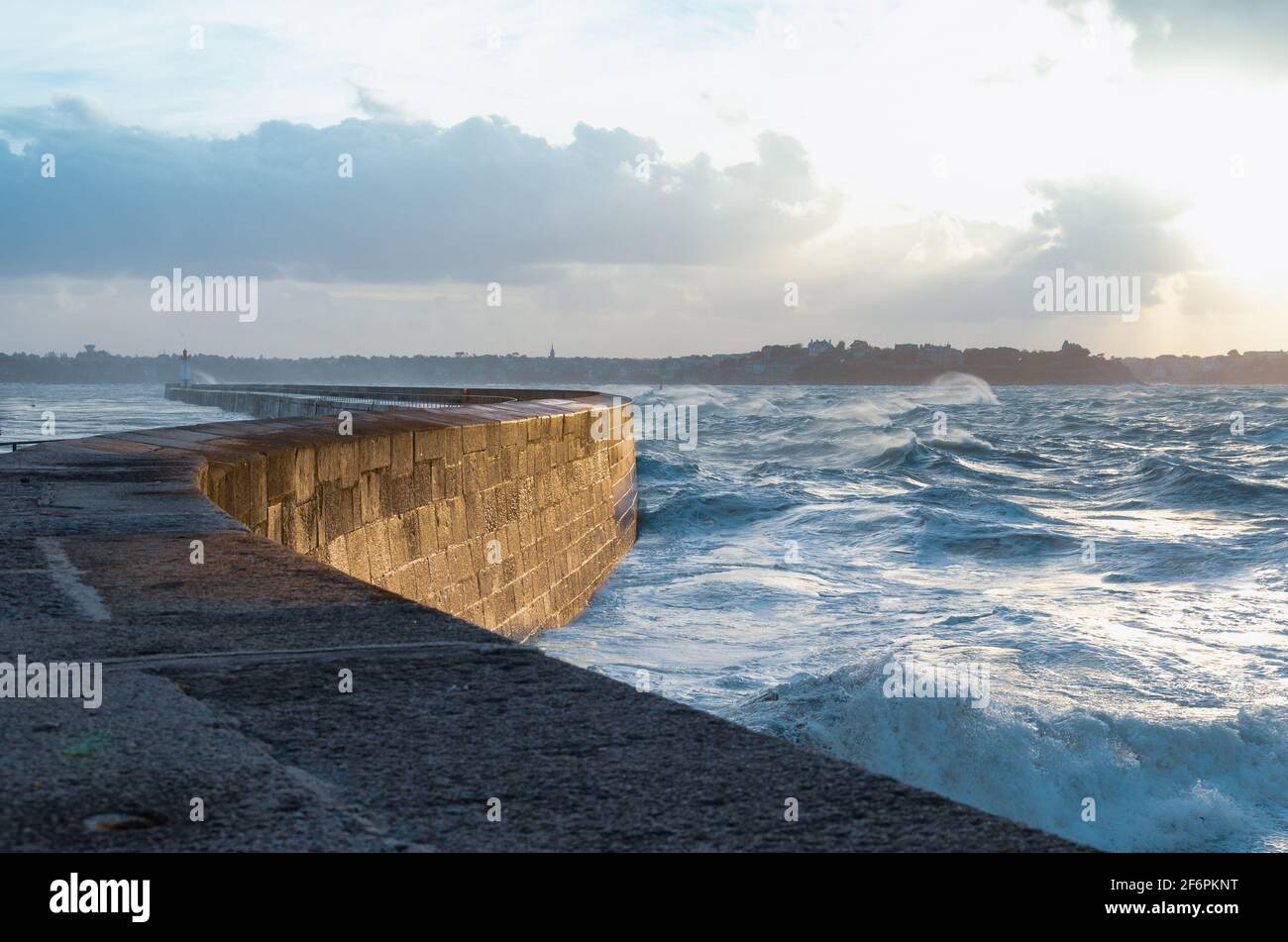 Big waves crushing on curved stone pier, on stormy weather with vivid