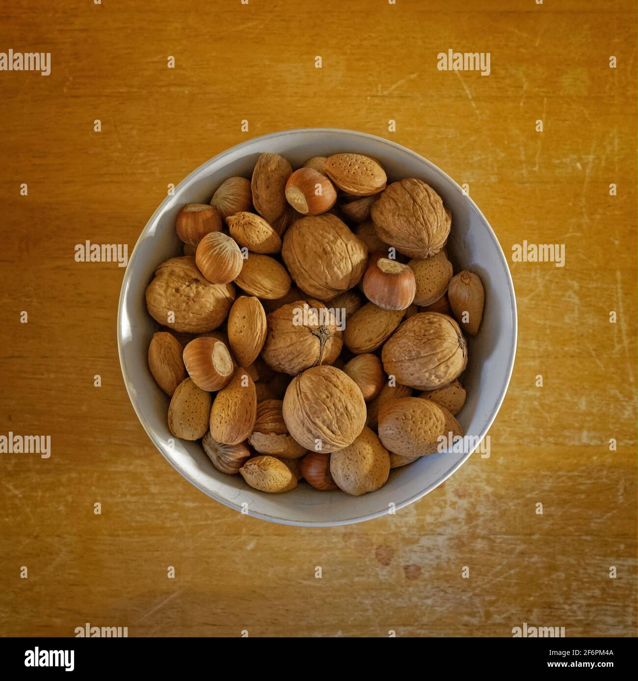 White bowl of unshelled nuts on a worn wooden table, seen from above. Stock Photo