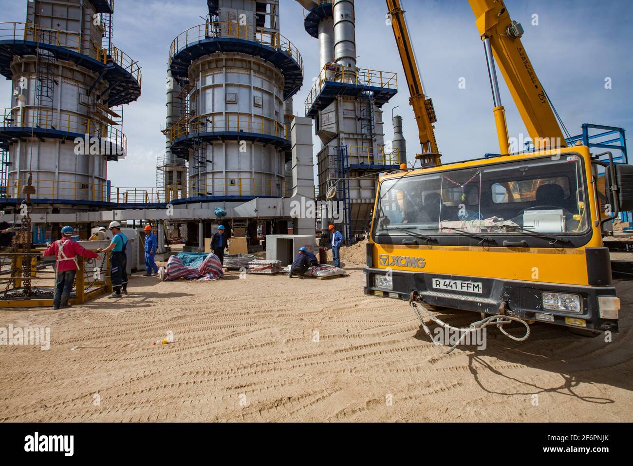 Aktau, Kazakhstan - May 19, 2012: Construction of asphaltic bitumen plant. Grey distillation tower complex, workers and yellow hydraulic hoist. Stock Photo