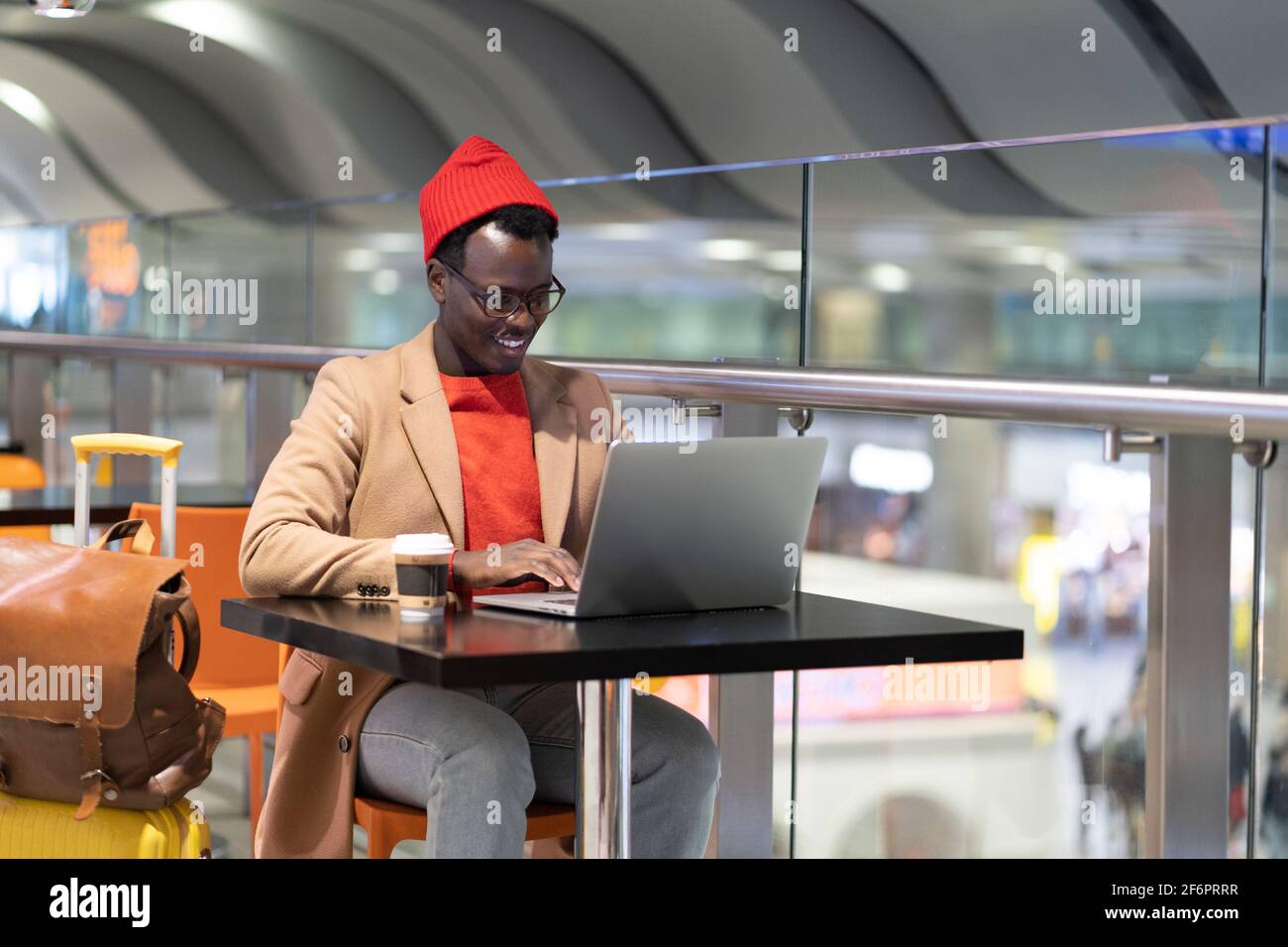 African traveler man sitting at cafe table in airport, works remotely on laptop waiting for a flight Stock Photo