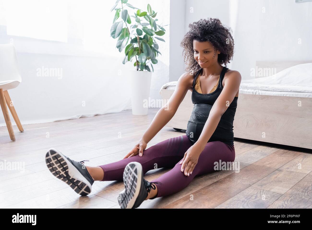 Smiling pregnant african american woman training on floor in bedroom Stock Photo