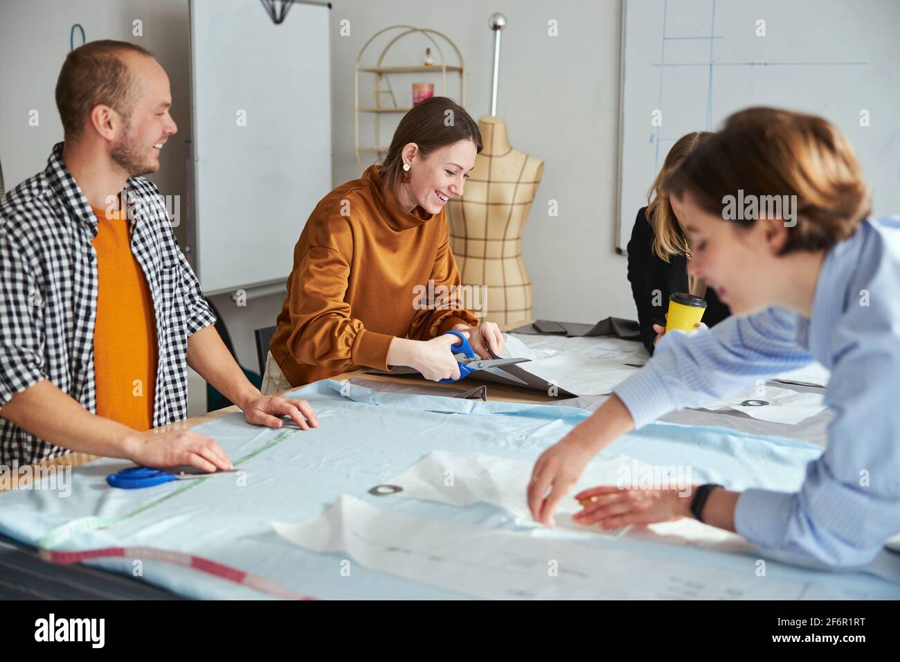 Cheerful couturiere laughing while cutting fabric material Stock Photo