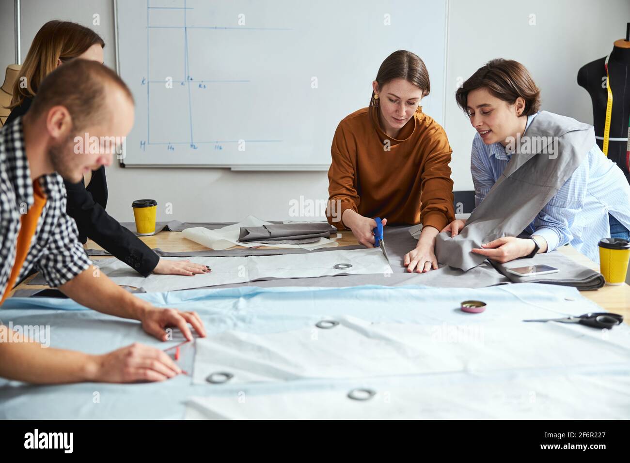 Woman tailor showing fabric sheet to co-worker while cutting Stock Photo