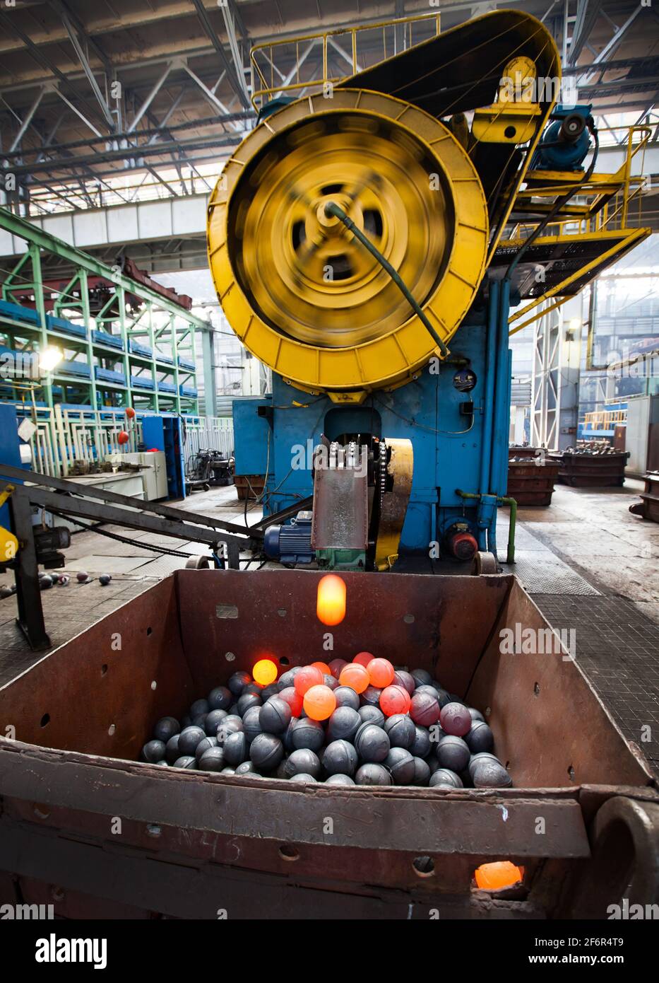 Bearing production plant workshop. Mechanic press for stamping steel balls. Red hot balls falling in metal hopper. Stepnogorsk, Kazakhstan. Stock Photo