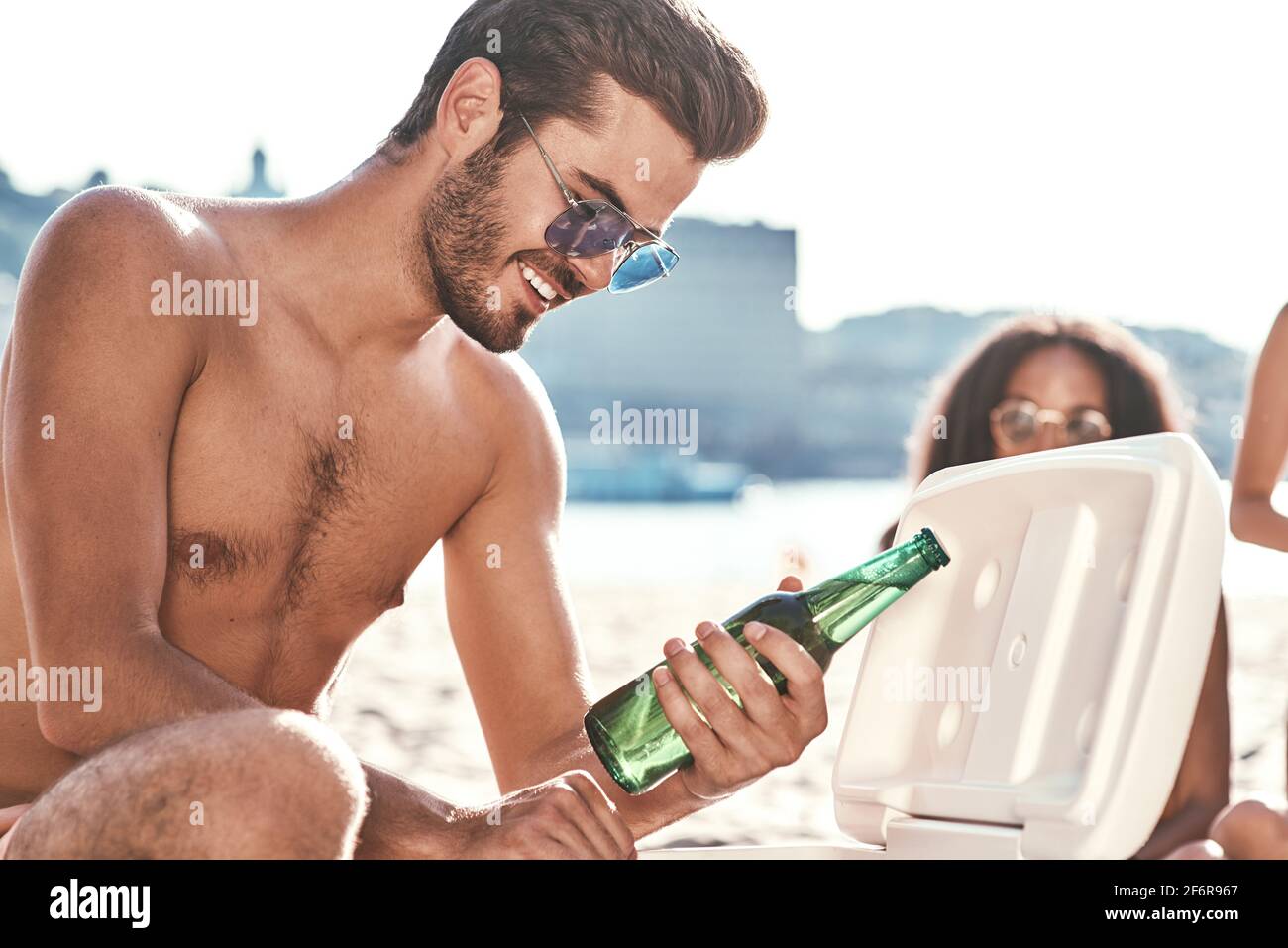 Enjoying carefree time with friends. Cheerful young people spending nice time together while sitting on the beach and drinking beer Stock Photo