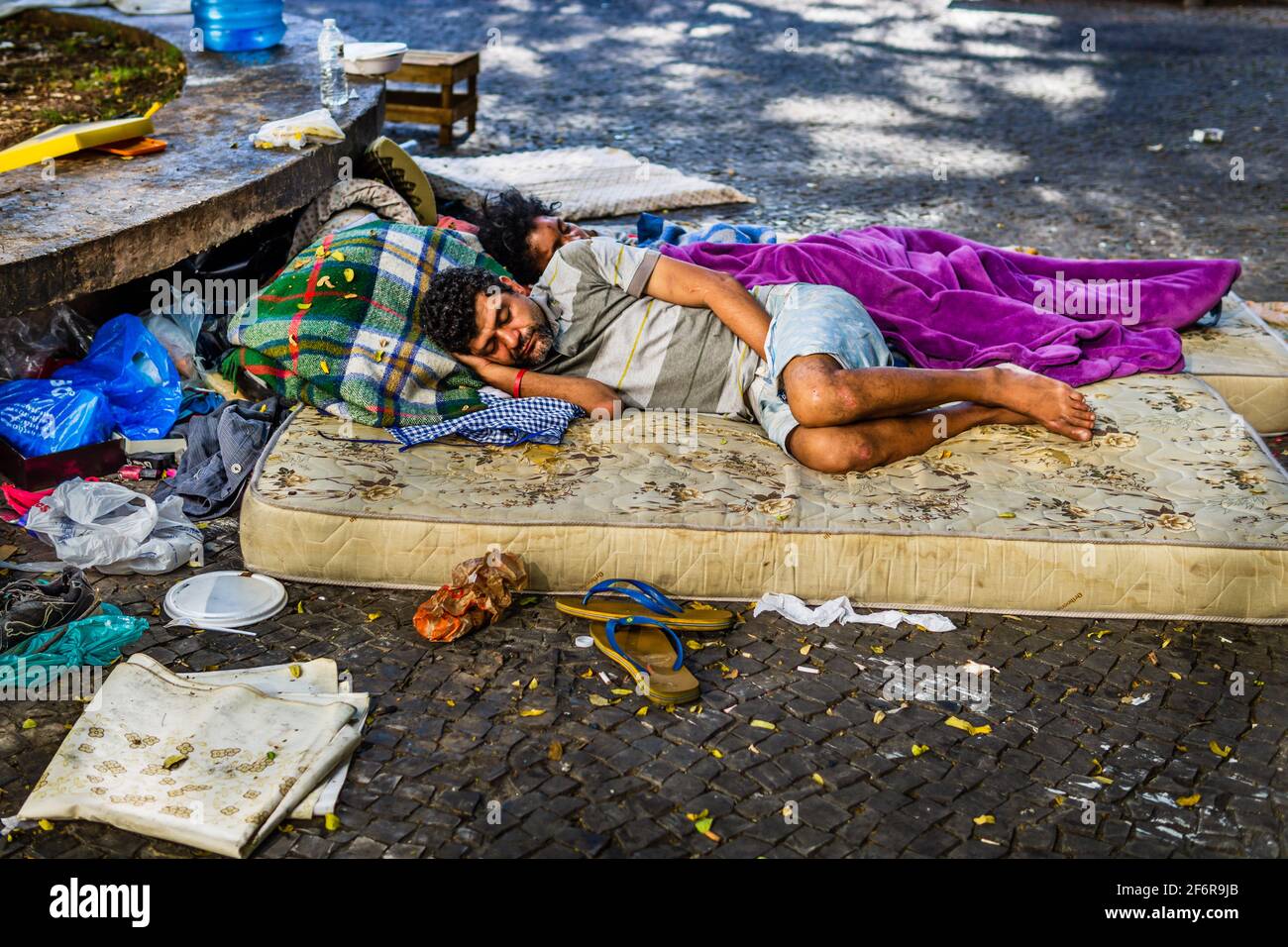 Brazilian homeless couple sleeping on a mattress on the sidewalk of a street in Belo Horizonte, Brazil, surrounded by trash and dirty belongings. Stock Photo