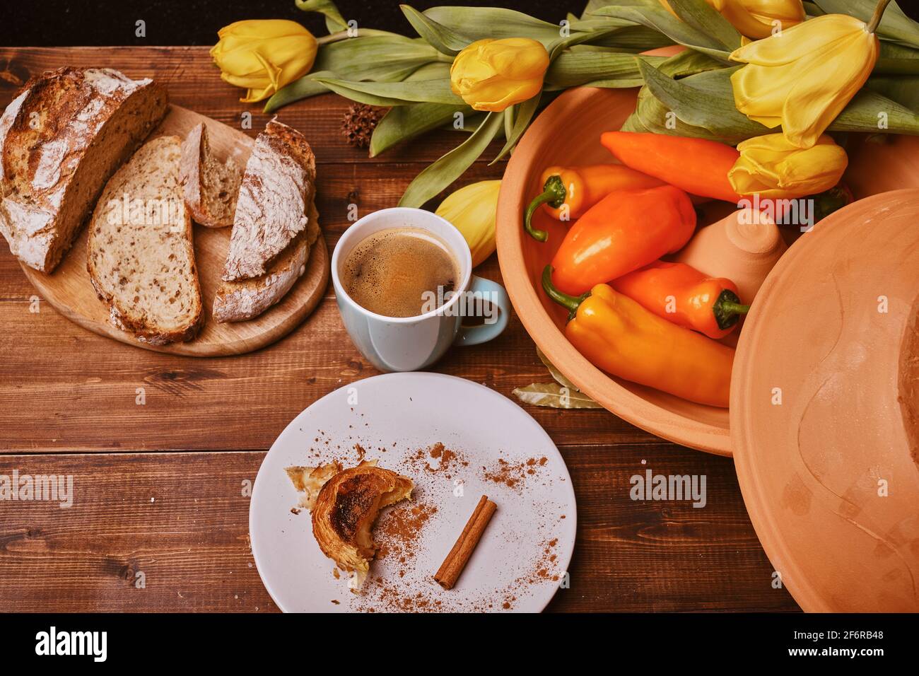 rustic table, with warm and cozy lighting shows cup with coffee, cinnamon, on the table you can also see peppers and a large ceramic bowl in raw color Stock Photo