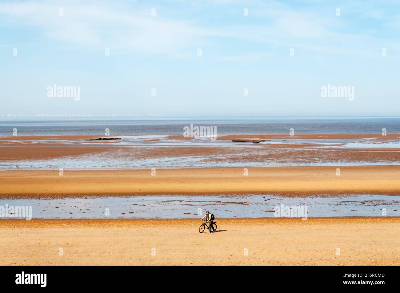 A man pushing a bike along an otherwise deserted, empty beach at Holme-next-the-Sea on the North Norfolk coast. Stock Photo