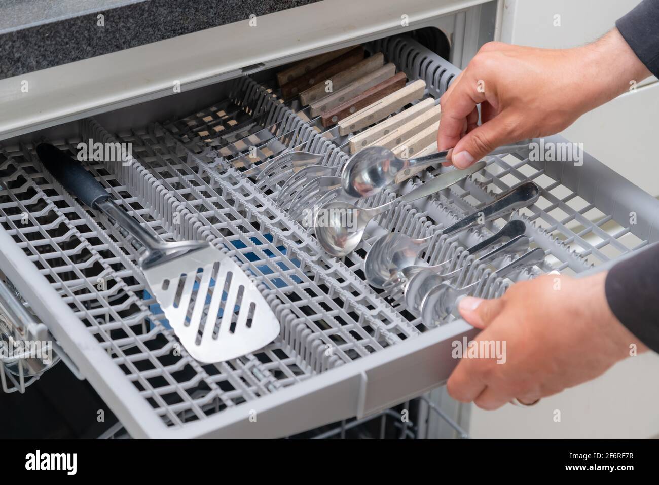 Close up of hand unloading dish washer in the kitchen. Person taking of  appliances of full shelf of dishwasher Stock Photo - Alamy