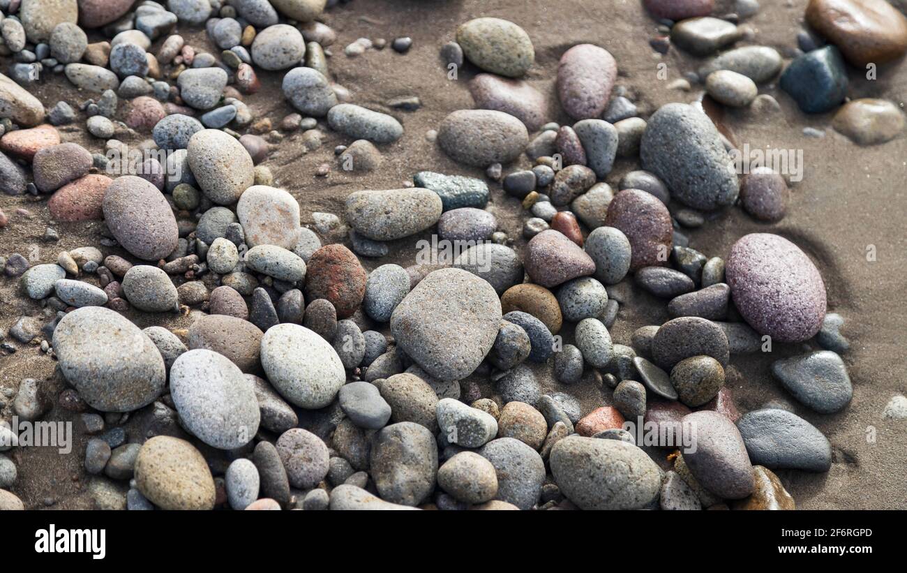 Smooth stones on brown beach sand Stock Photo