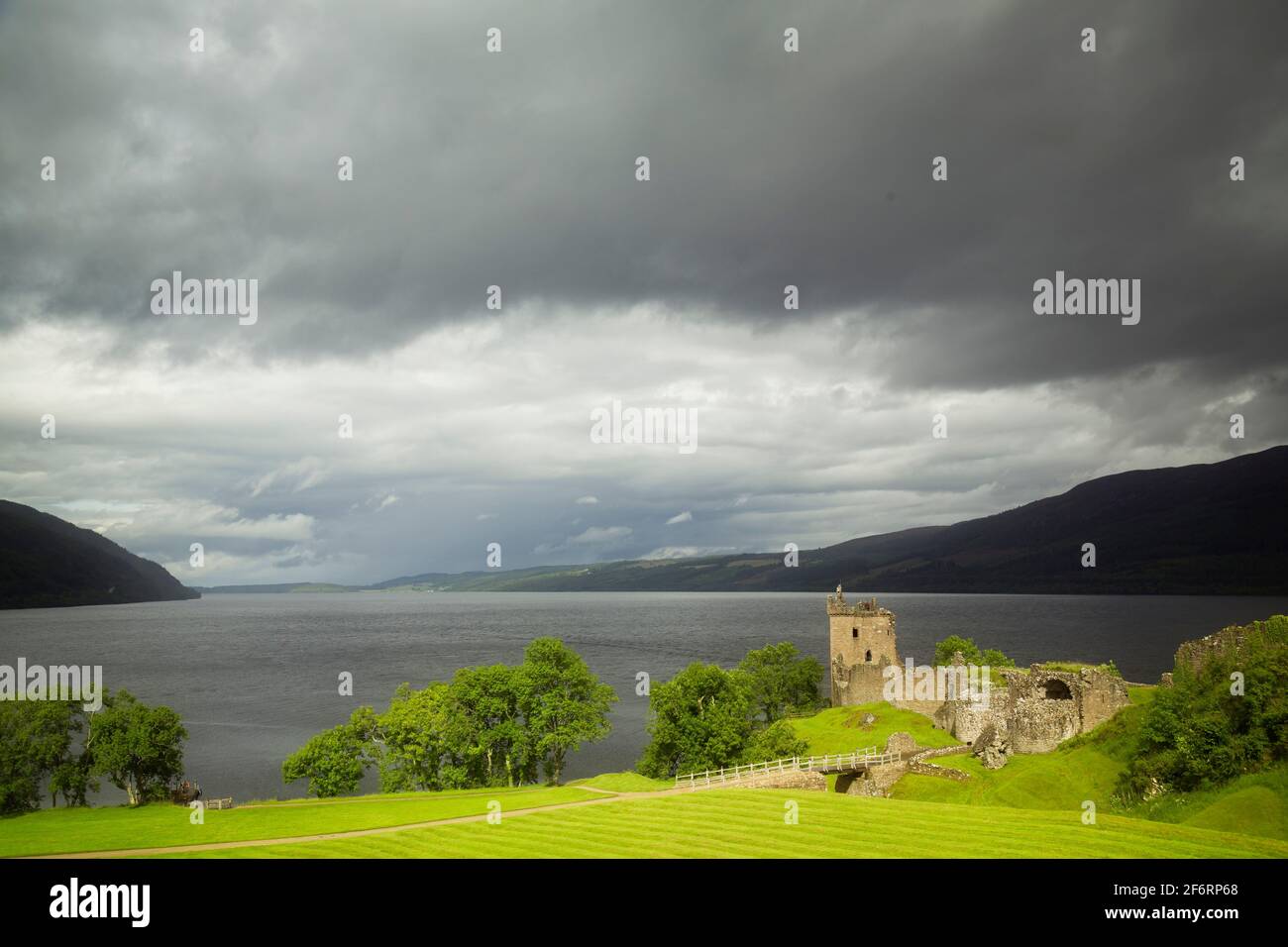 View of Urquhart Castle in sunlight with Loch Ness under dark clouds behind. Stock Photo
