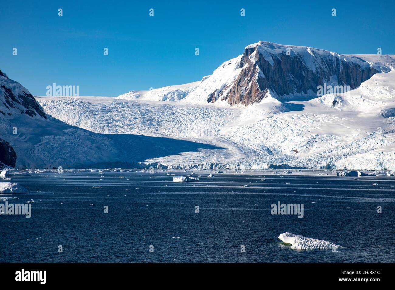 Glacier tongue between mountains covered with snow and ice flows into Antarctic sea. Stock Photo