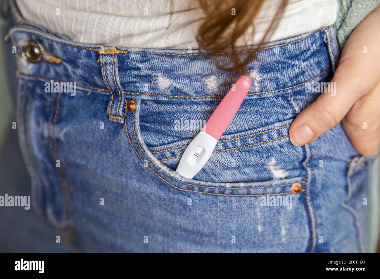 Young woman with positive pregnancy test in pocket of jeans close-up motherhood happiness modern retro background. Stock Photo