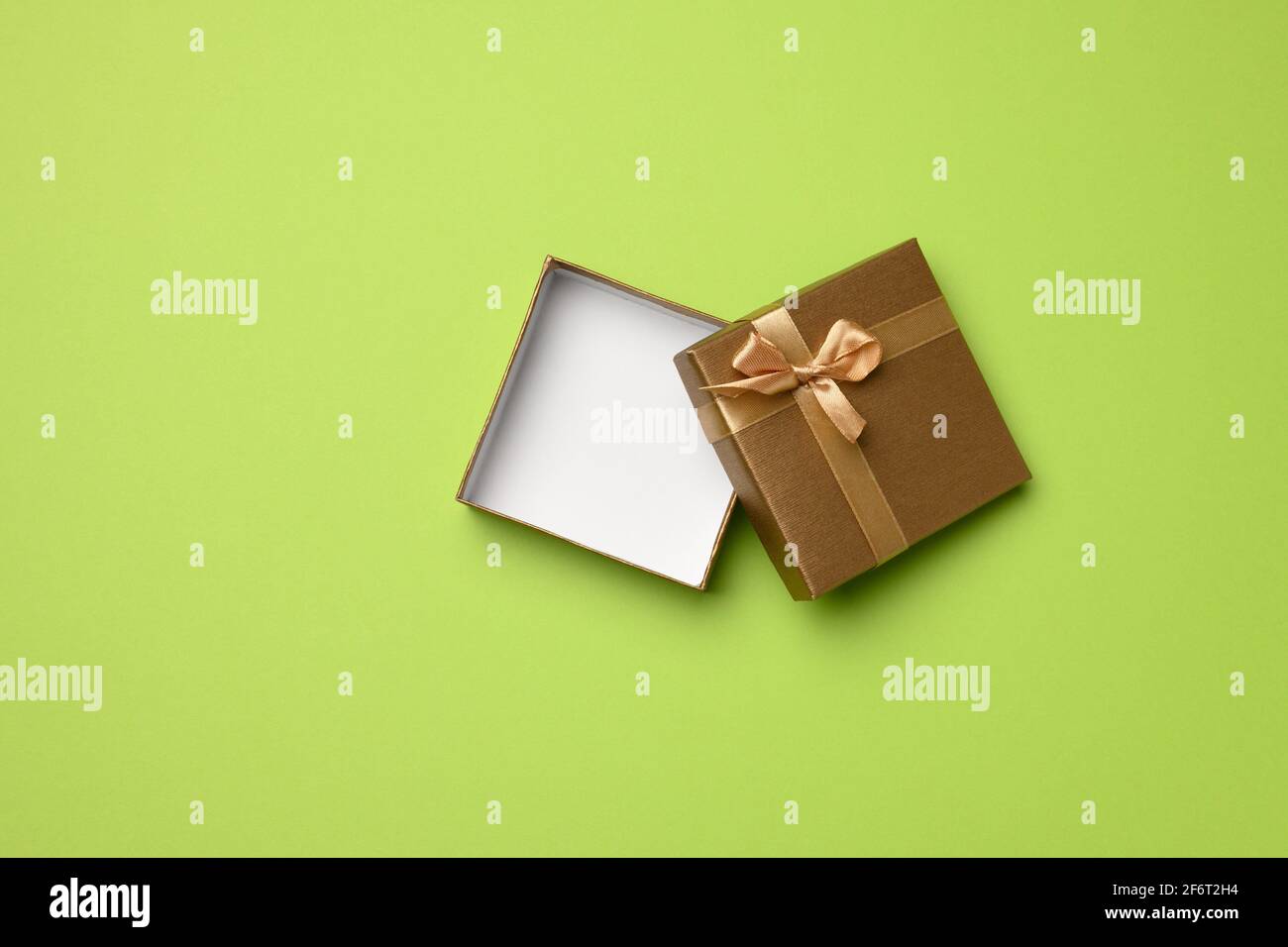 empty square golden box with cardboard bow on green background, gift open, top view. Stock Photo