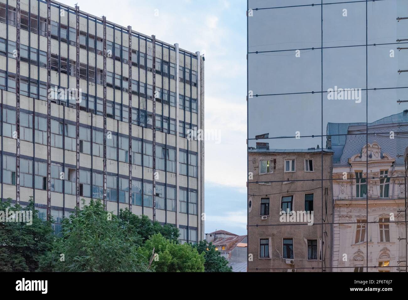Old classical buildings reflected in the modern glass building, with the socialist modernism building in the background, Bucharest, Romania Stock Photo