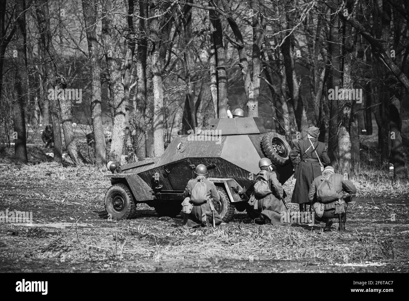 Group Of Reenactors Dressed As Russian Soviet Red Army Soldiers Of World War II Go On Offensive Under Cover Of Armored Soviet Scout Car. Historical Stock Photo