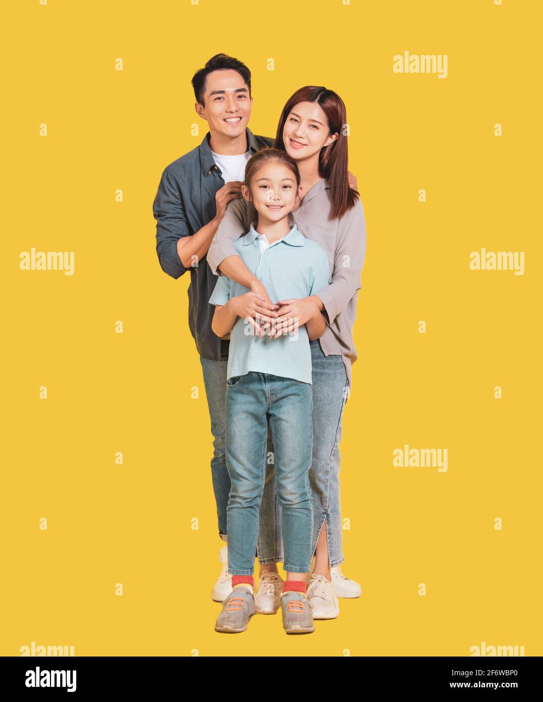 Happy Asian young family with one child standing embracing and smiling at camera isolated on yellow Stock Photo