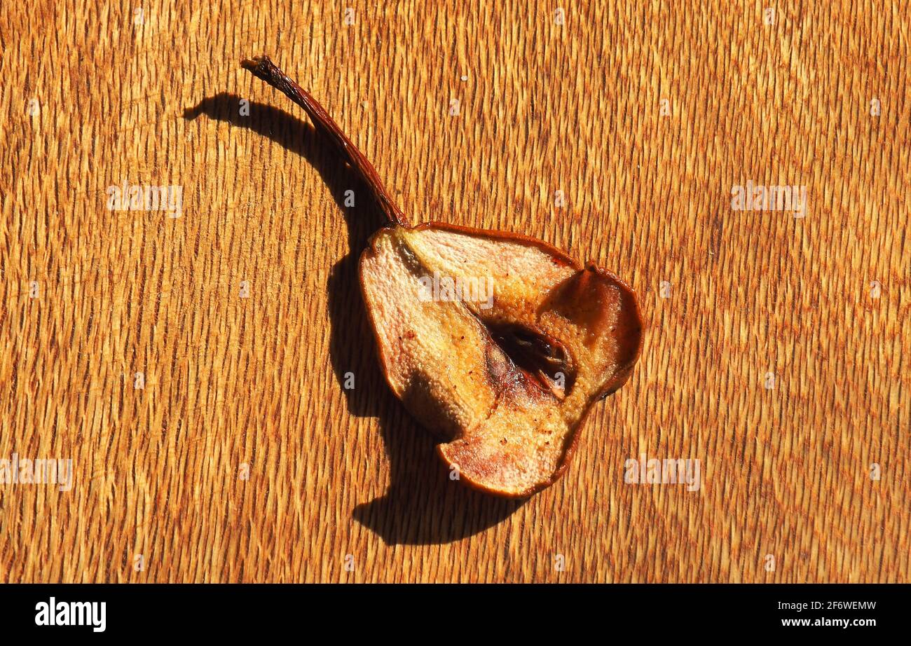 A thin slice of a dehydrated brown pear on a wooden cheese board Stock Photo