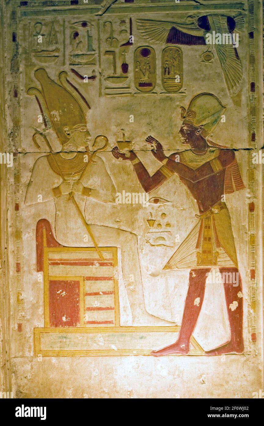 An ancient Egyptian painted hieroglyphic carving of the Pharoah Seti making a religious offering to the god of the underworld - Osiris. Niche at the T Stock Photo