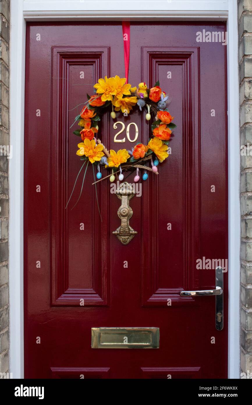 An orange and yellow floral Easter wreath on a red, paneled, wooden front door.  Door furniture (number, handle, letterbox) is in brass. Stock Photo