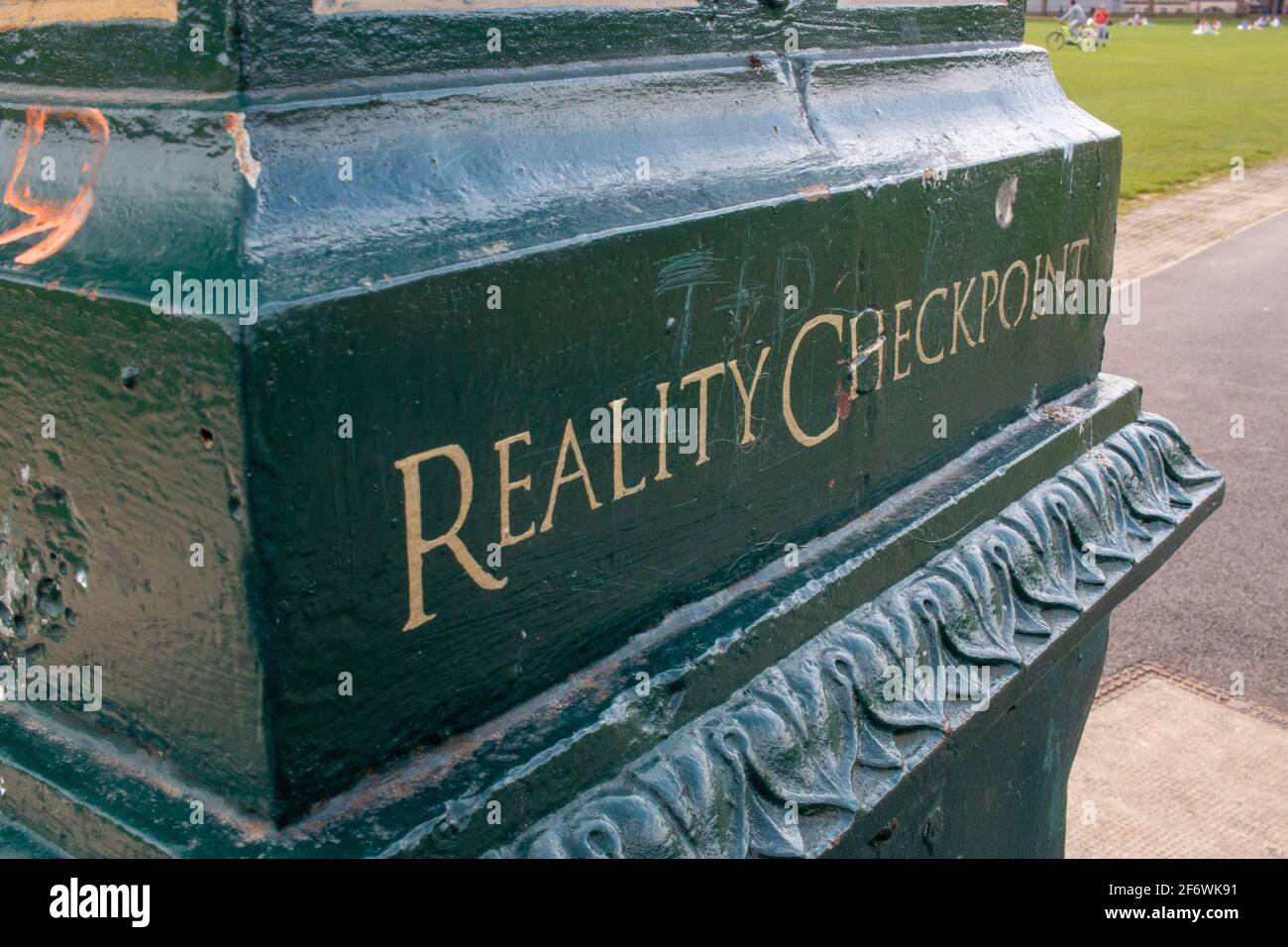 Reality Checkpoint sign engraved on the central cast iron lamp post on Parker's Piece, Cambridge, UK.  Gold lettering on a green metal background. Stock Photo