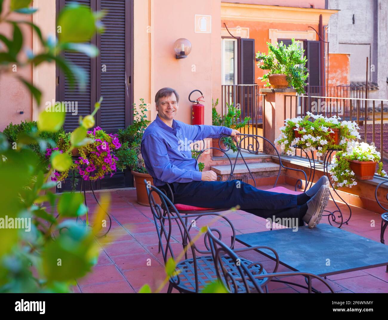 Smiling Caucasian man in forties resting on rooftop patio covered in red tiles in Italy Stock Photo