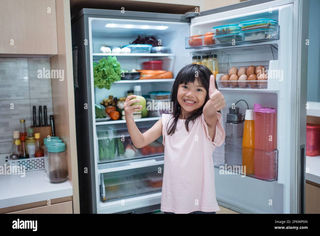 asian girl open fridge door drinking a bottle of juice Stock Photo
