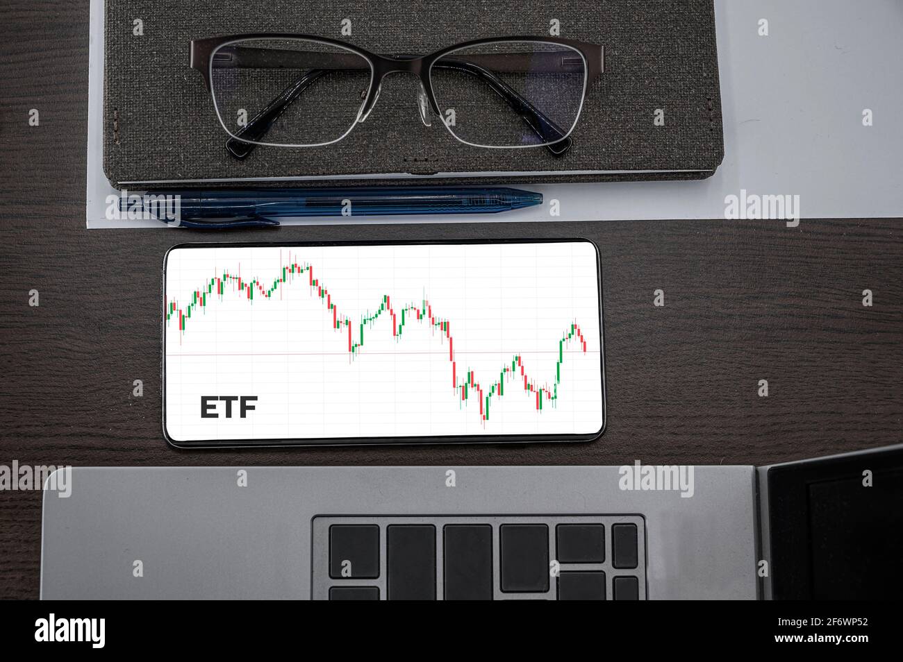 Buy or sell ETF concept. Exchange Traded Fund. Top view of stocks price candlestick chart in phone on table near laptop, notepad and glasses with insc Stock Photo