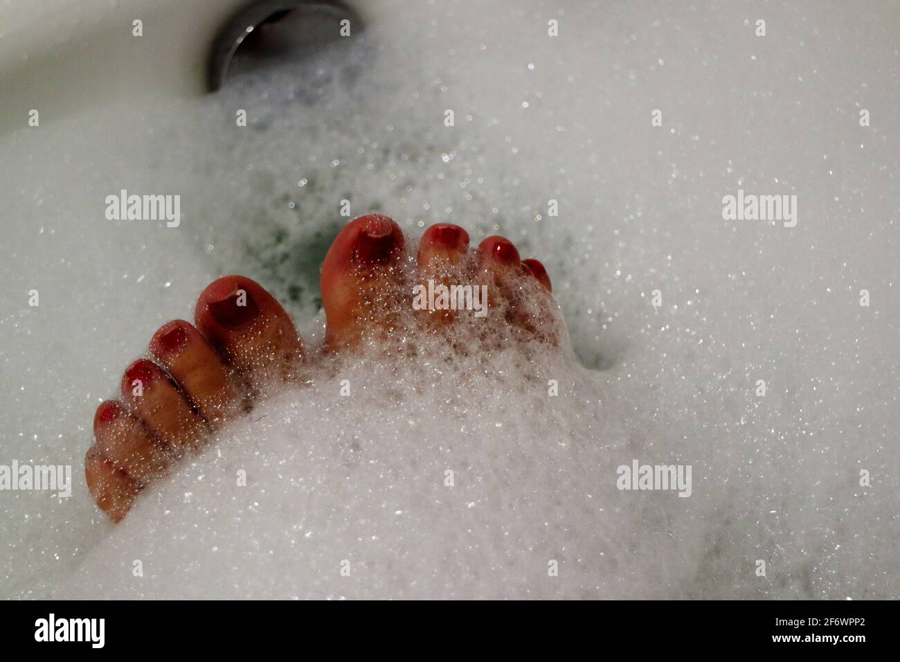 Close up of woman's red painted toe nails having a relaxing bubble bath