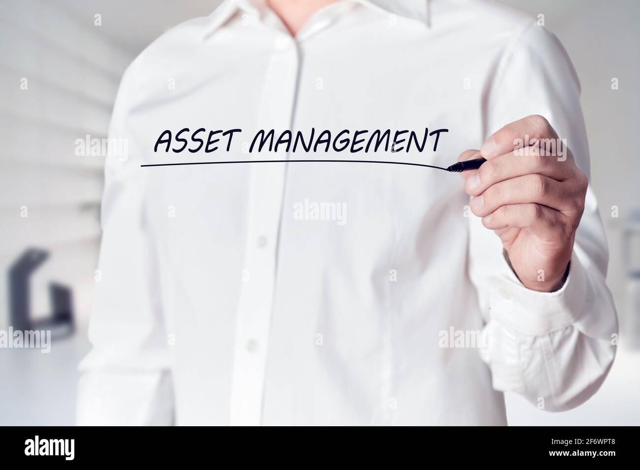 Businessman hand holds a pen and underlines the words asset management on virtual screen. Managing business assets concept. Stock Photo