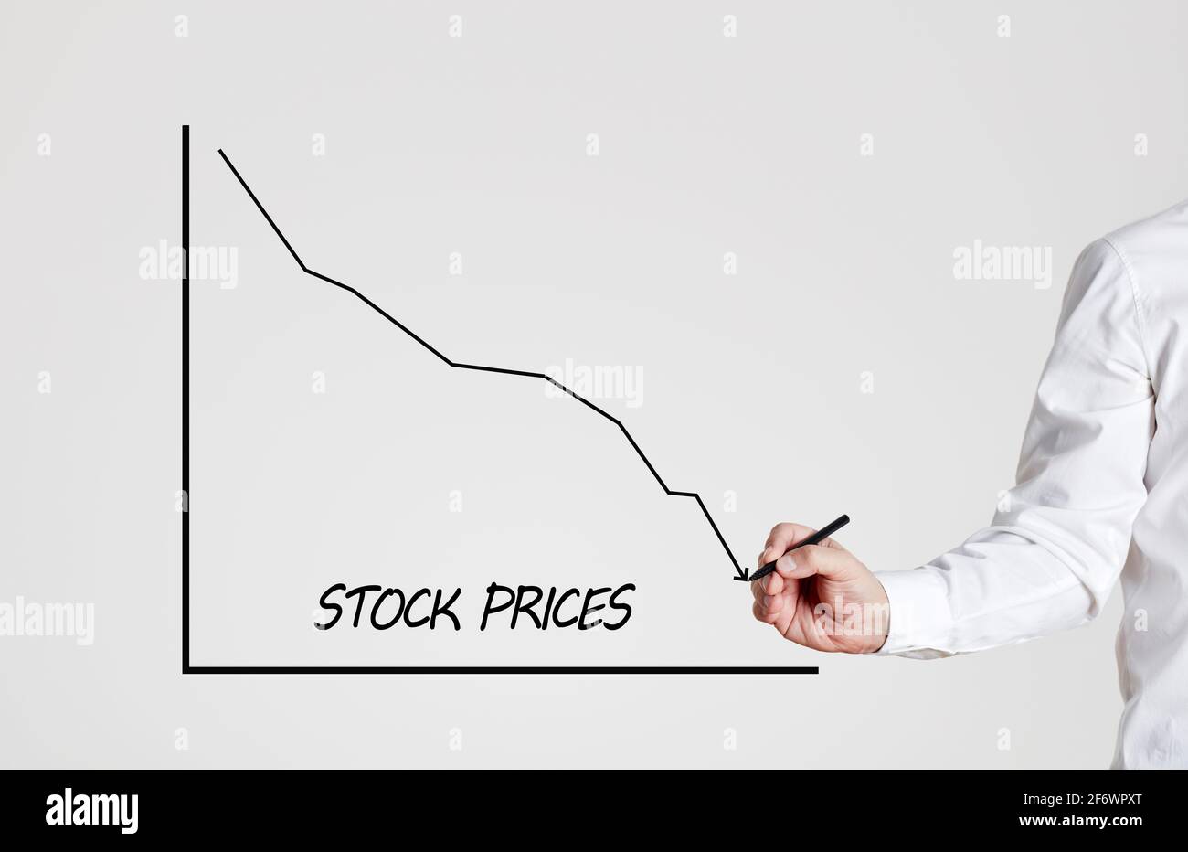 Businessman draws a declining line graph with the word stock prices. Economic crisis and falling stock market prices concept. Stock Photo