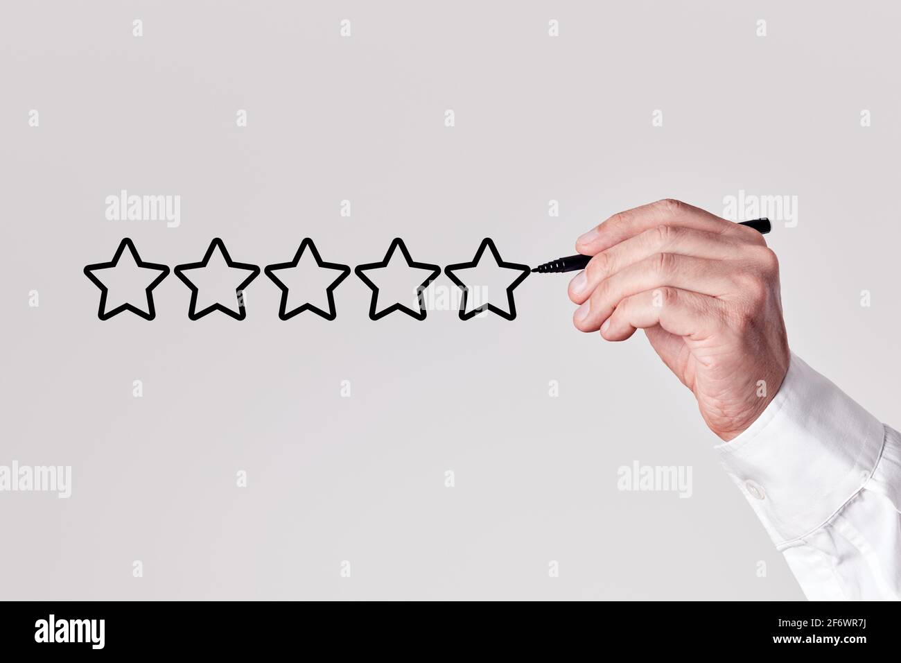 Businessman with a pen draws five stars on gray background. Customer satisfaction or rating concept. Stock Photo