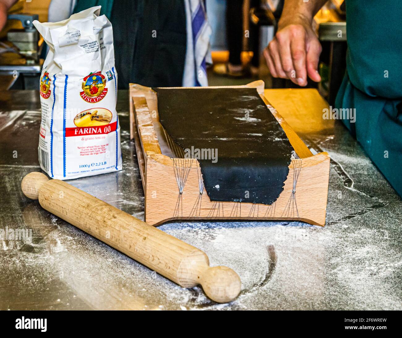 A sheet of squid-ink pasta dough is laid over the carraturo, the traditional Abruzzo pasta cutter, in the kitchen of Hotel Endsleigh in West Devon, England. A chef's hand reaches for it, the wooden rolling pin already in place to press the dough through the device's wires and cut it into thin strips. Stock Photo